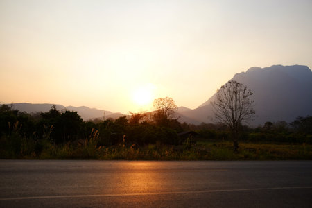 beautiful of the sky and the sunset behind the mountains along the country road in Thailandの写真素材