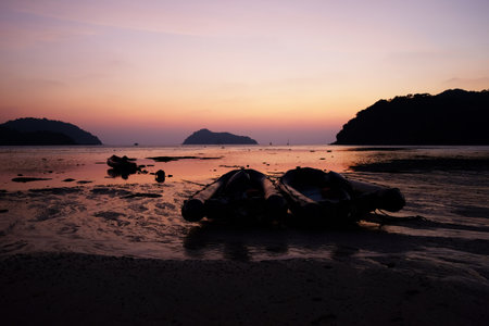 Two rubber boats on the beach with stunning sunset over a tranquil beach with vibrant violet and pink colors reflecting on the sea water in Thailandの写真素材