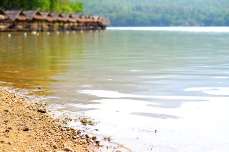 Close up sand on riverbank with thatched building by the river and tropical forest background