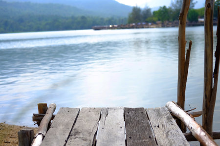 Rustic wooden bridge on riverbank with thatched building by the river and tropical forest backgroundの写真素材