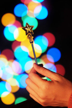 Close up woman hand holding star shaped wand in light bokeh on Celebrate Christmas background. Festive elegant abstract background