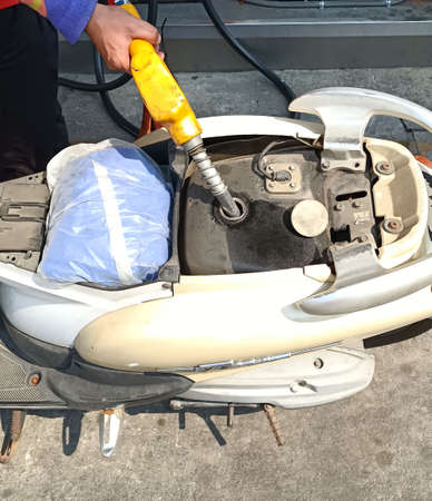 Hand fuel nozzle in pouring to old motorcycle at gas stationの写真素材
