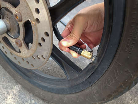 Asian man inflates old motorcycle wheels for road safetyの写真素材