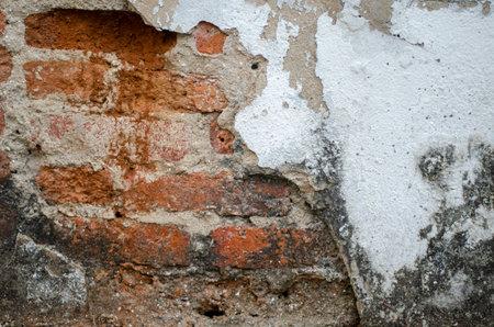 Old cement wall cracked to reveal red bricks inside, poor quality construction.の写真素材