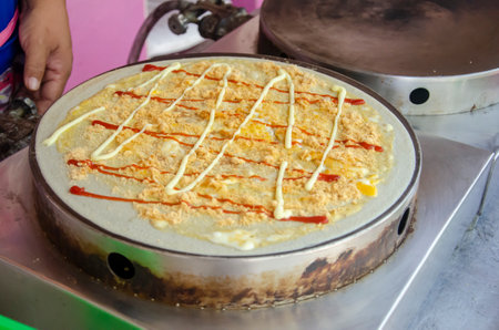 Cooking crepe dessert with topping, egg, dried shredded pork, ketchup, mayonnaise in street food...