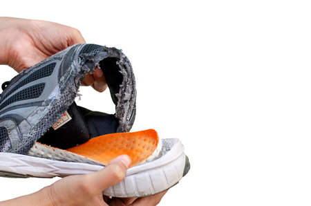 Hand holding an old, broken black shoe behind the heel of the shoe isolated on white background with clipping pathの写真素材