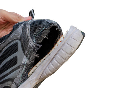 Hand holding an old, torn black shoe behind the heel of the shoe isolated on white background with clipping pathの写真素材