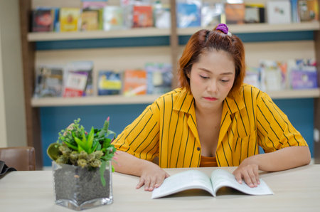 Young woman sitting attentively reading a book in the libraryの写真素材