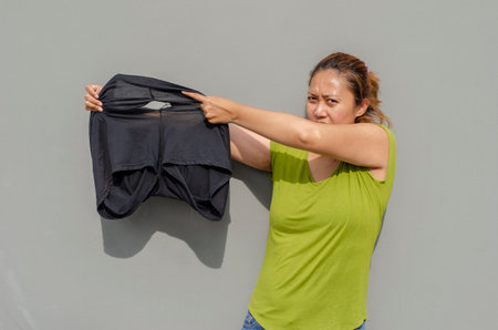 Asian women showing his old black pants torn buttock after a long time of use. grey background