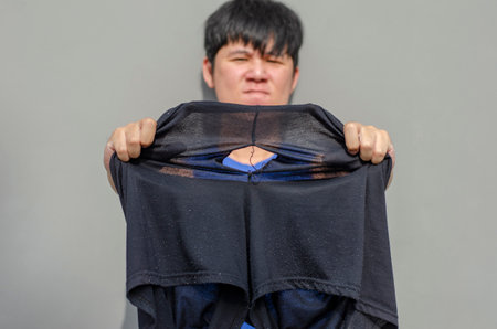 Asian man showing his old black pants torn buttock after a long time of useの写真素材