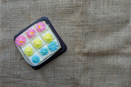 Fresh and delicious bento mini vanilla cupcakes with whipping cream pastel colors. on brown fabric background. Top view with copy spaceの写真素材
