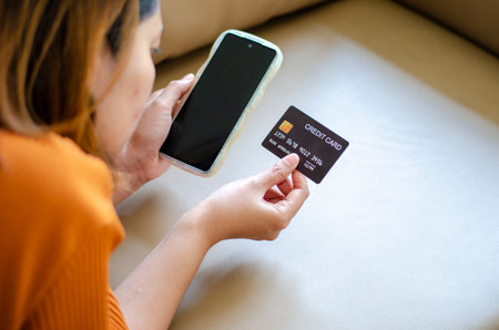 Asian woman holding black credit card lying on sofaの写真素材