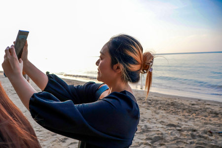 Happy asian woman standing on the beach use smartphone selfie on the sea, tree, blue sky background. Travel Rayong Province, Thailand.の写真素材