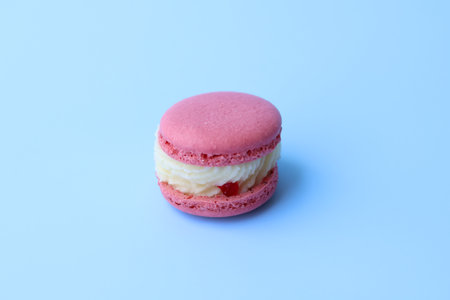 Only one colorful pink macaron with generous cream fillings on a blue background. Traditional dessertの写真素材
