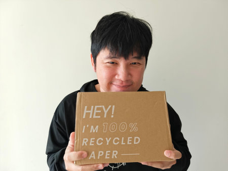 A young man with a smiling face holds a cardboard box made from recycled paper, embodying an eco-friendly concept.の写真素材