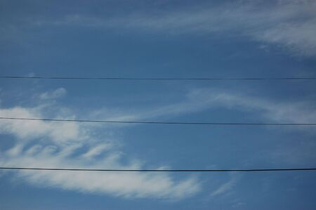 A classic blue skyline with fluffy white clouds, with black phone wires dominating view             ...
