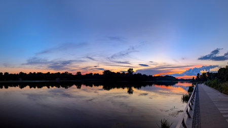 A panoramic dome of cirrus clouds. An arch of magical purple sunset with yellow and orange reflections from the sun is reflected in the calm waves of the river. A calming evening spectacle.の写真素材