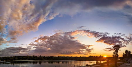 An orange evening sky at sunset. Flattened flakes of cloud against a yellow and blue sky. The sun's...