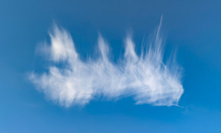 A lone, vanishing feather steam. Cirrus cloud structures fly overhead against a clear blue sky. Soft, wispy clouds, evoking peace and freedom.の写真素材