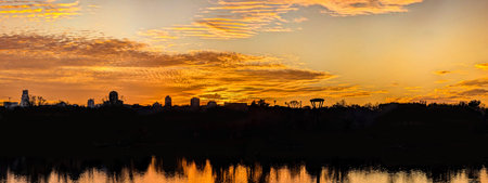 A panoramic dome of gold cirrus clouds. An arch of magical yellow sunset with golden and orange reflections from the sun is reflected on calm waves of a river. Calming evening spectacle.の写真素材