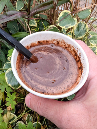 Hot chocolate in disposable cup ready to drink. Top view of a paper cup. A hot drink with a funnel-like texture and bubbles. Invigorating cocoa and cream against a backdrop of warm greenery.の写真素材