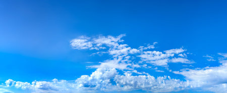 A panorama of cumulus clouds against a blue sky. A summery, serene landscape. The cloud's smooth movement copy space for banner text. Clear background with tiny white fluffy cloud.の写真素材