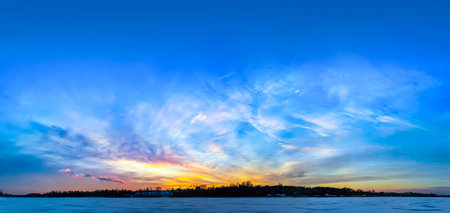 Landscape in winter after the sunset. Colorful clouds near the hidden sun on horizon. Big space for text blue background above fabulous yellow orange weather. Cold river under ice.の写真素材