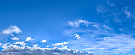A panorama of cumulus clouds against a blue sky. A summery, serene landscape. The cloud's smooth movement copy space for banner text. Clear background with tiny white fluffy cloud.の写真素材