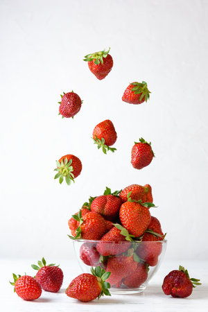 Fresh strawberries in a glass bowl with flying berries on a white background.の写真素材