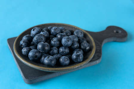 Fresh organic blueberries in a ceramic saucer on a ceramic board on a blue backgroundの写真素材