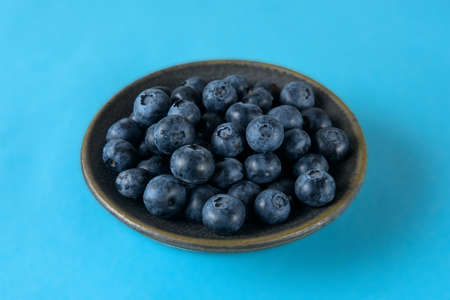 Fresh organic blueberries in a ceramic saucer on a blue backgroundの写真素材