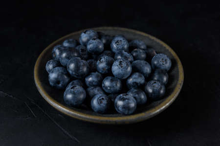 Fresh organic blueberries in a ceramic saucer on a black backgroundの写真素材