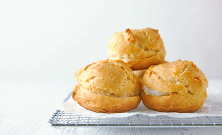Home-made profiteroles on a metal grate on a white wooden background.の写真素材