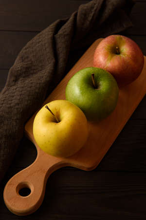 Yellow, green and pink apples lie on a wooden board next to a brown cotton napkin on a brown wooden background.の写真素材