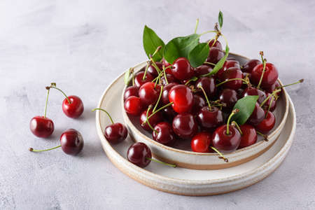 Berries of fresh cherries in two light ceramic plates on a gray concrete background. Horizontal. close-up.の写真素材