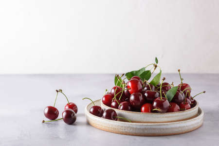 Fresh cherries in two light ceramic bowls on gray concrete and white background. Horizontal. Place...