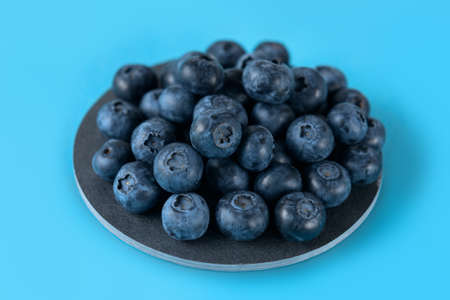 Fresh blueberries on a gray round ceramic board on a blue background. Horizontal.の写真素材