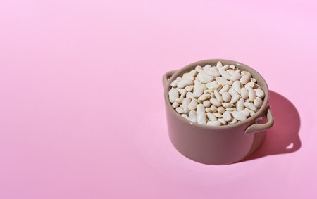 Dried white beans in a gray bowl isolated on a pink background with a deep shadow. Close up, copy space.の写真素材