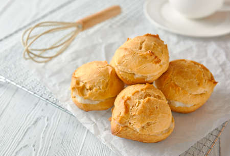 Homemade profiteroles or eclairs on a metal grid. There is a whisk next to it, there is a cup on a saucer behind it. Traditional French dessert. Close up, copy space.の写真素材