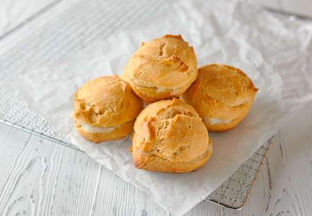 Homemade profiteroles or eclairs on a metal grid on a light wooden background. Classic French dessert. close-up.の写真素材