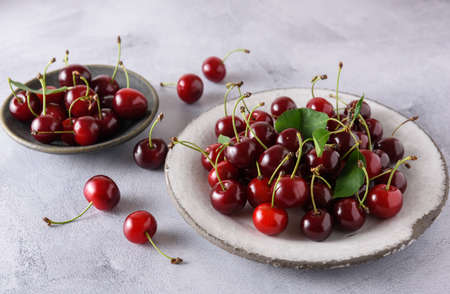 Fresh ripe cherries in a white ceramic plate. Behind is a cherry in a gray ceramic plate. close-up.の写真素材