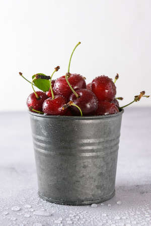 Cherry in drops of water in an iron bucket on a light background. close-up.の写真素材