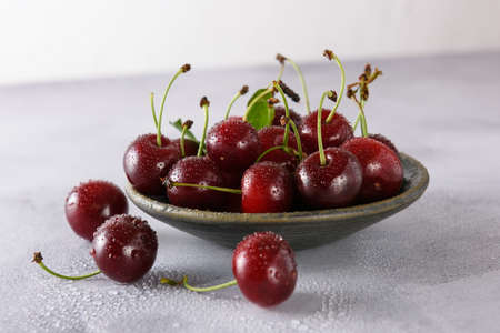 Fresh red cherry in drops of water in a gray ceramic saucer on a light background. close-up.の写真素材