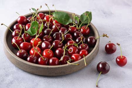 Fresh red cherries in a gray ceramic plate. There are several cherries on the table nearby. close-up.の写真素材