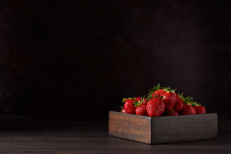 Fresh strawberries in a square wooden bowl on a brown wooden table. brown background. Close up, copy space.の写真素材