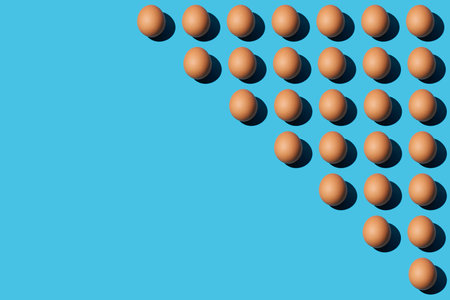 Trendy pattern of brown chicken eggs on a bright blue background with hard light and deep shadow. Minimal concept, diagonal copy space, close-up, top view.の写真素材