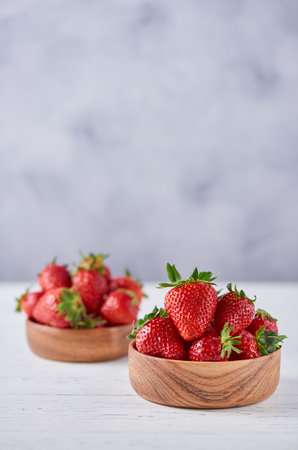 Two wooden bowls with ripe strawberries on a gray background. Vertical, copy space, close up.の写真素材