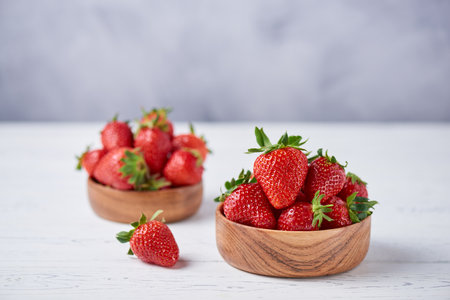 Fresh ripe strawberries in wooden bowls on a white wooden table. gray background. Horizontal, copy space, close up.の写真素材