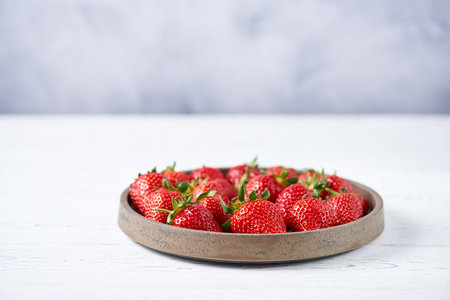Fresh red strawberries in a gray ceramic plate on a white wooden table. Horizontal, copy space, close up.の写真素材