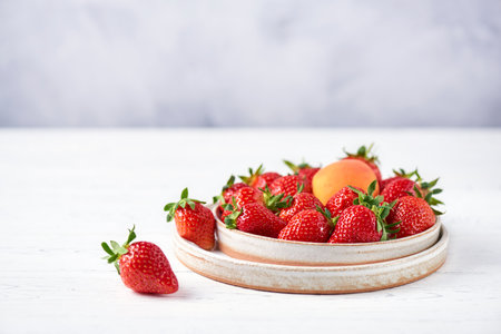 Fresh strawberries and apricot in two ceramic plates on a white wooden table and a gray background. Copy space, close-up.の写真素材